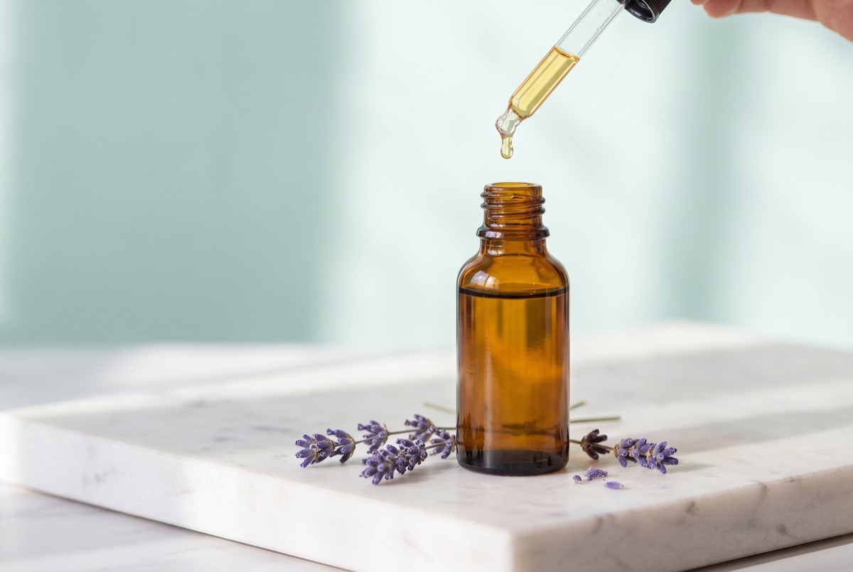 An amber glass dropper bottle of golden facial oil beside dried lavender