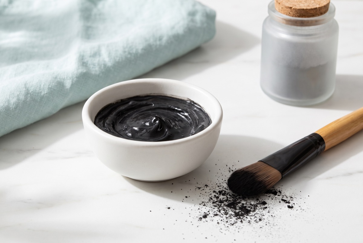 Black charcoal face mask paste in a white bowl with an applicator brush